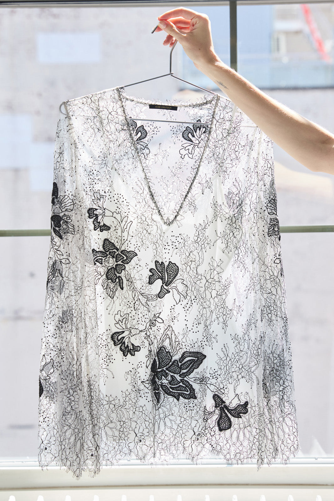 Lace top with black floral embroidery on a hanger against a window background