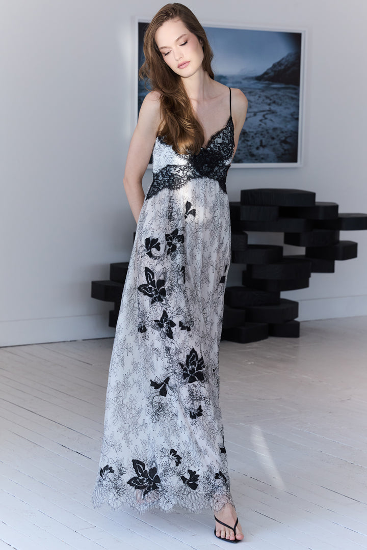 Woman wearing a long, elegant dress with black floral patterns in a minimalistic room.