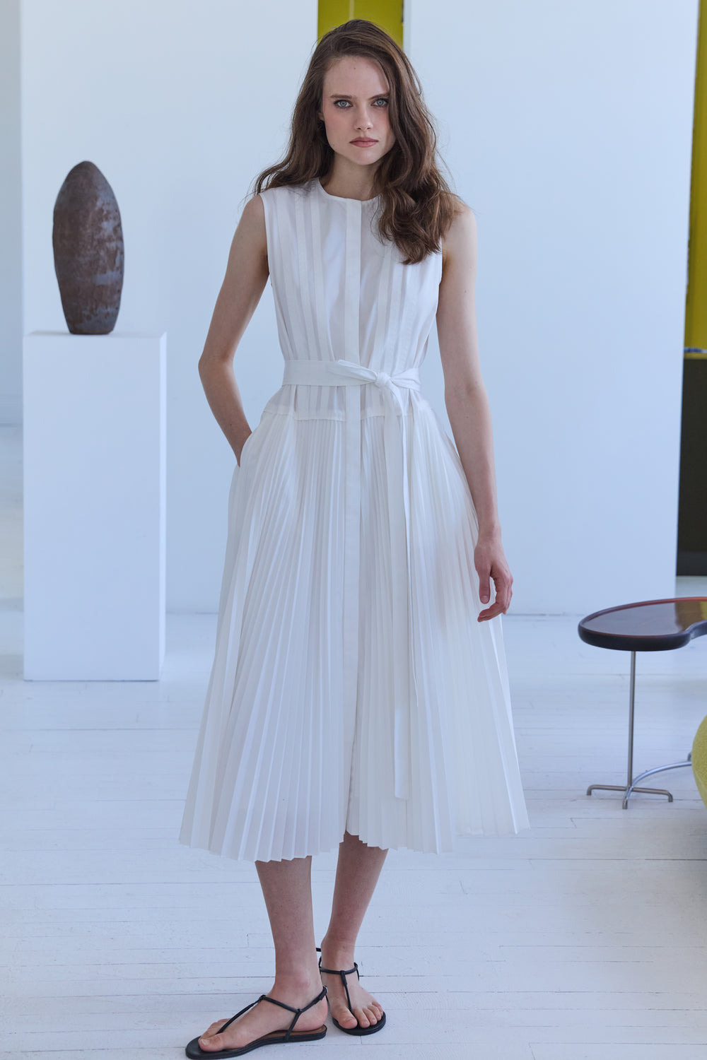 Woman wearing a white pleated dress in a minimalistic room.