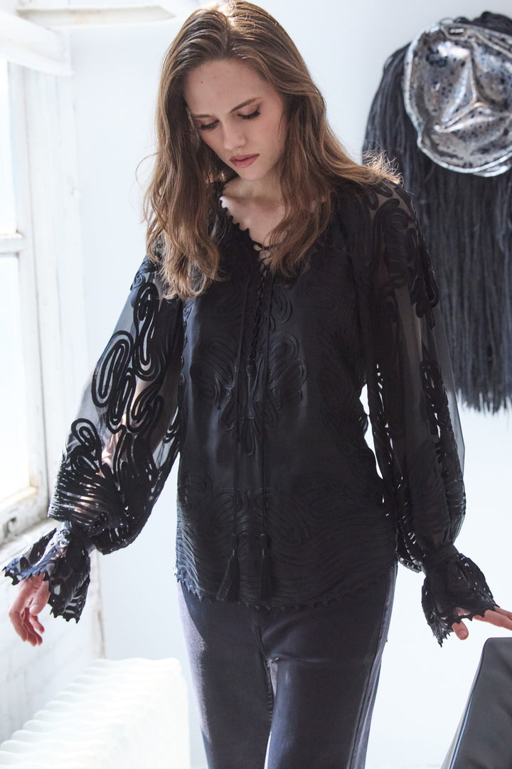 Woman wearing a black textured top with long sleeves in a white room.