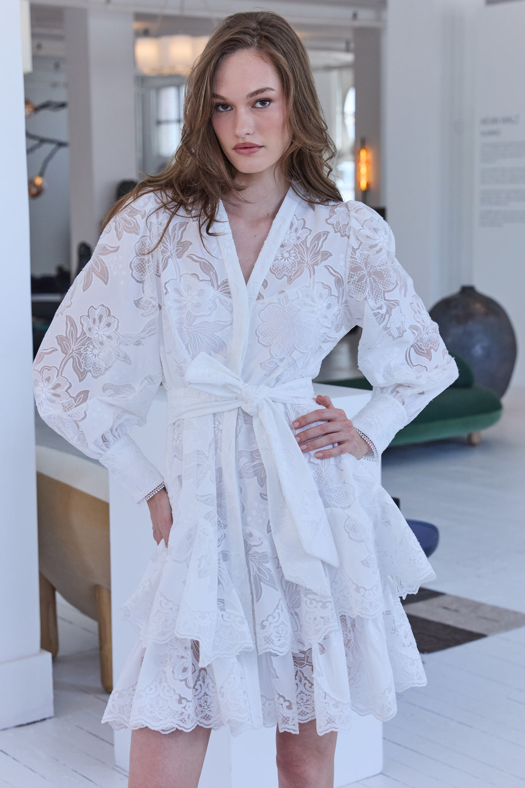 Woman wearing a white lace robe in a bright room.