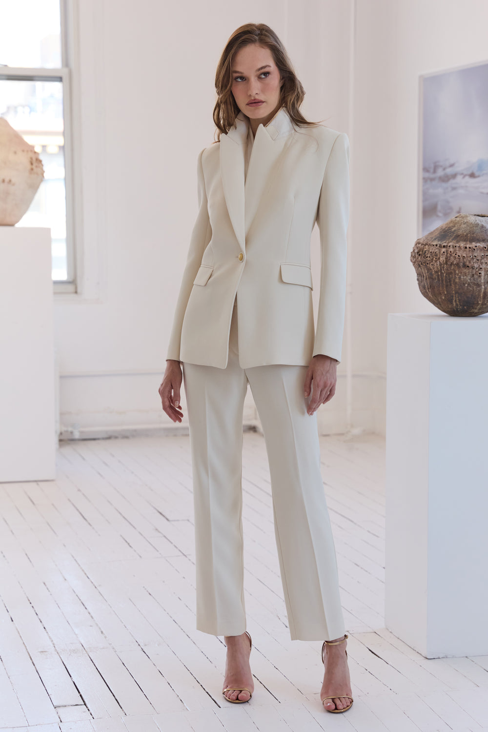 Woman wearing a cream suit in a bright room with white walls and wooden floor.
