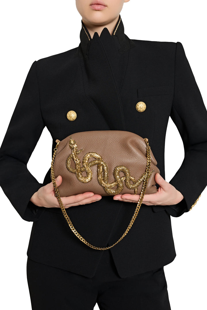 Structured snake leather clutch with gold jeweled serpent embellishment, gold chain strap; front view on model.