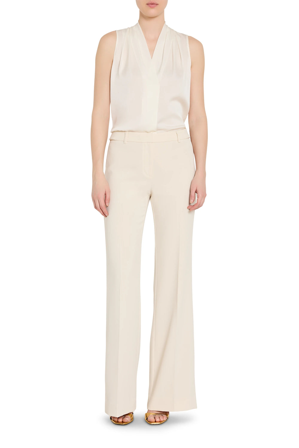 Person wearing a white sleeveless top and cream pants on a white background