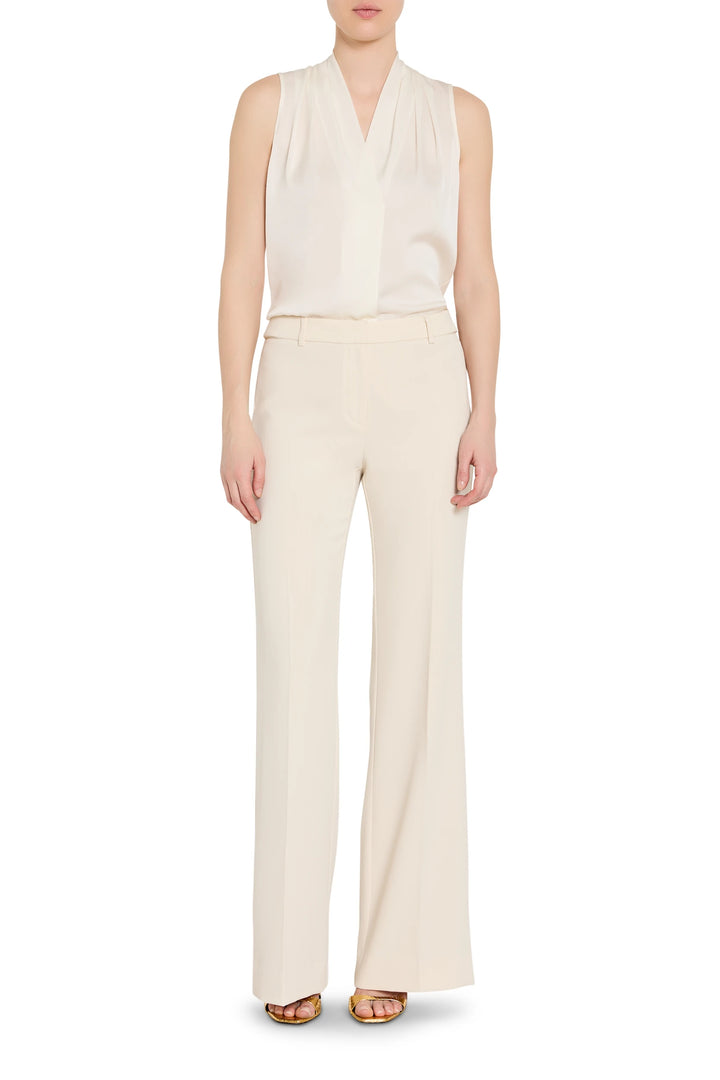 Person wearing a white sleeveless top and cream pants on a white background