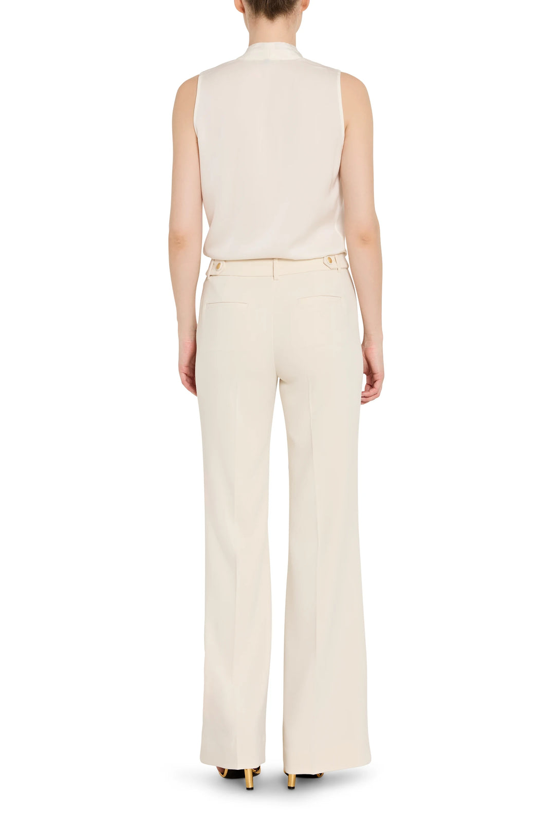 Person wearing a sleeveless beige top and high-waisted pants on a white background