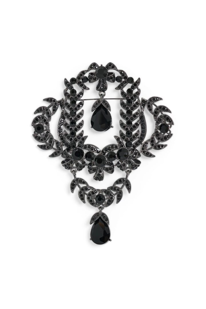 Heirloom-inspired brooch with black gemstone, filigree edges, and crystal teardrop pendant. Front view on white.