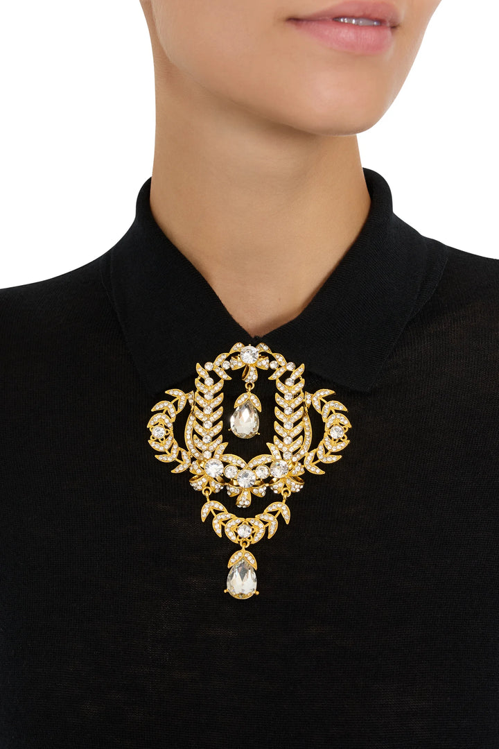 Large, heirloom-inspired gold brooch with crystal embellishment; sculptural construction. Front view on model.