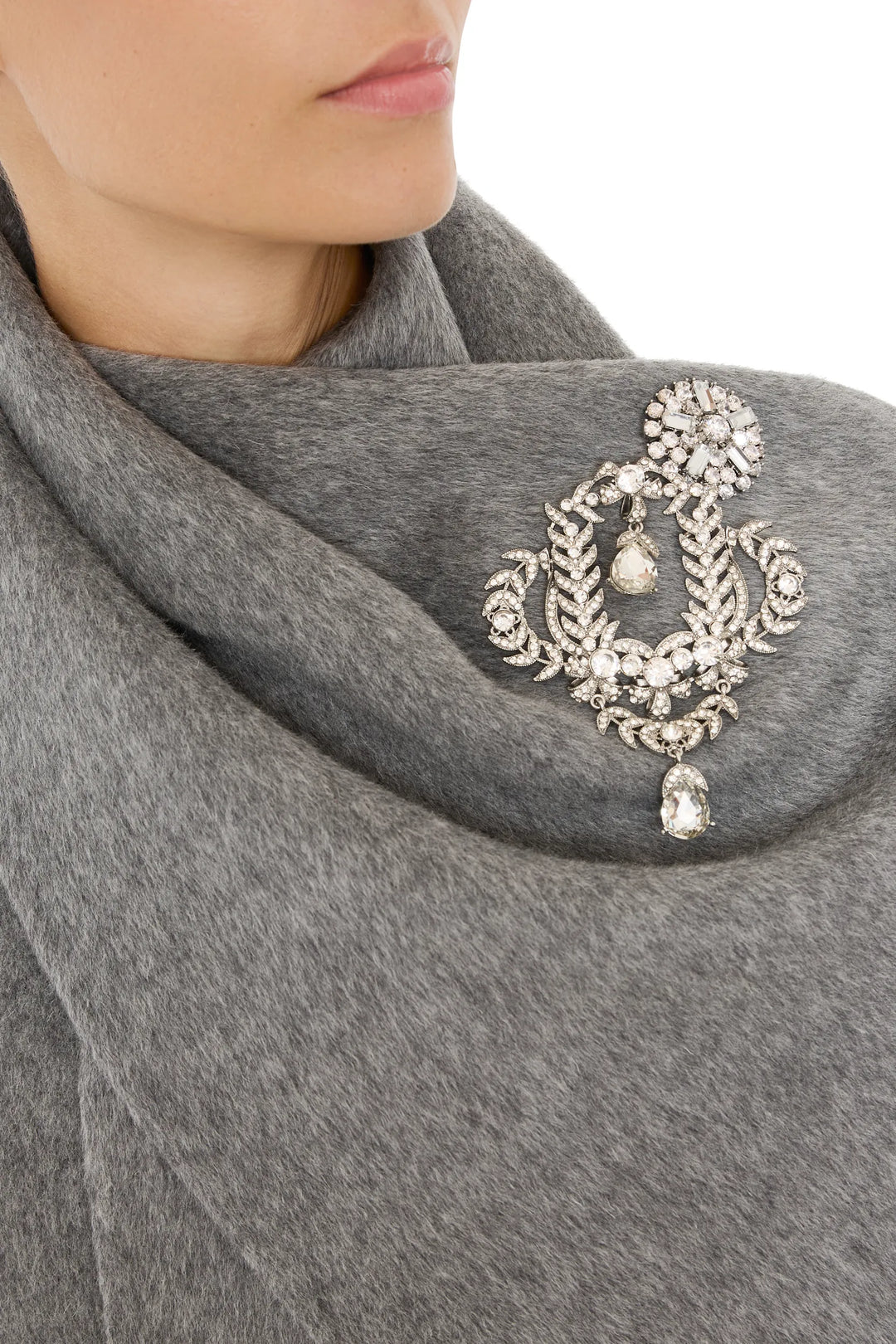 Oval brooch with intricate metalwork and central gemstone; classic silhouette. Front view on model.