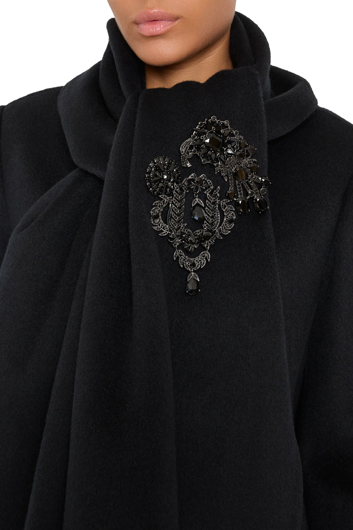 Oval brooch with intricate metalwork and gemstone accents, classic construction, front view on model.