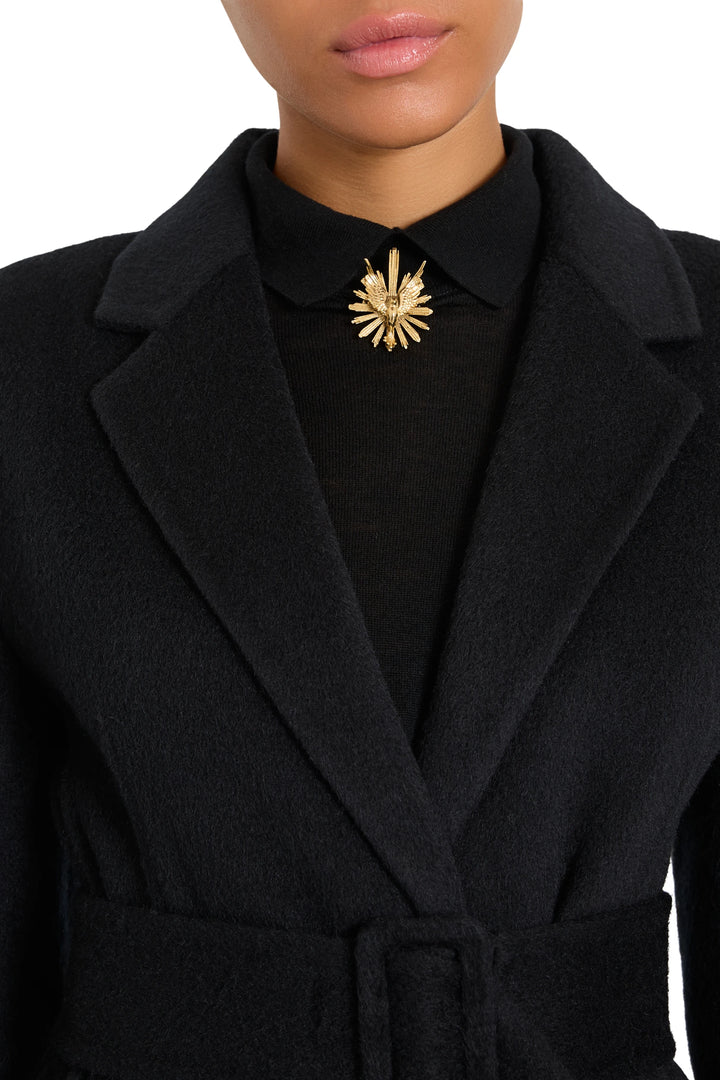 Round brooch with sculpted metal silhouette, intricate engraving detail at center. Front view on model.