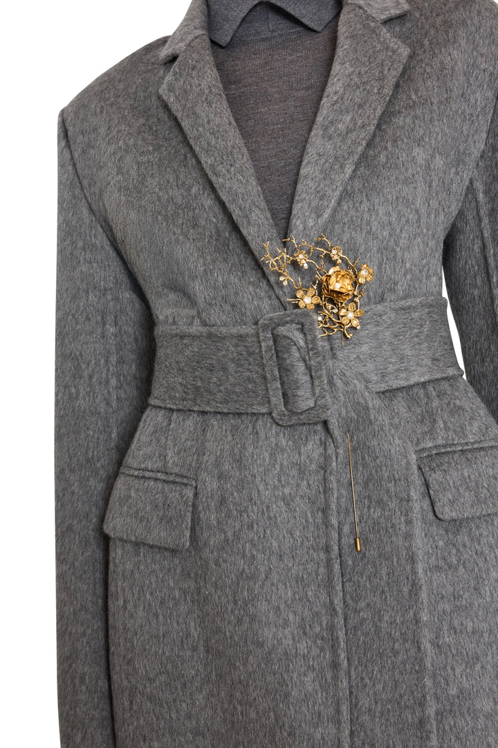 Gray belted coat with tailored silhouette and waist brooch accent, structured construction; front view on model.