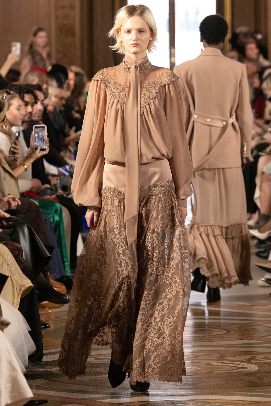 Sheer lace blouse with hand-embroidered detailing, high neckline, and puff sleeves; front view on model.