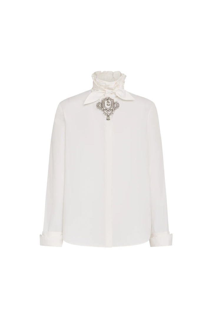 Poplin shirt with ruffled neck, jeweled brooch, structured silhouette, button placket. Front view on white.