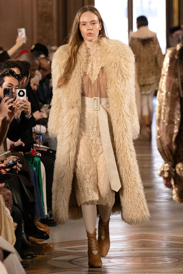 Long faux Mongolian coat with belted waist, textured plush fabric, structured shoulders; front view on model.