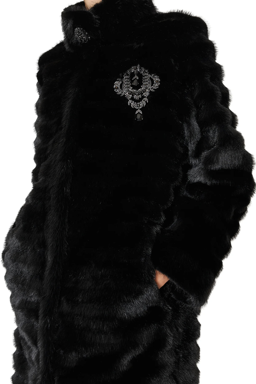 Long faux fur coat with jeweled brooch, straight silhouette, concealed closure, front pockets; side view on model.