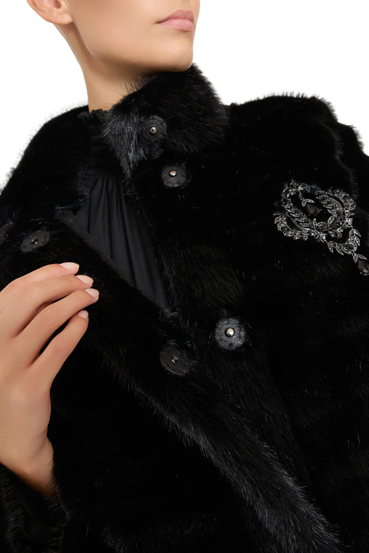 Long, plush faux fur coat with straight silhouette and jeweled brooch detail inside; front view on model.