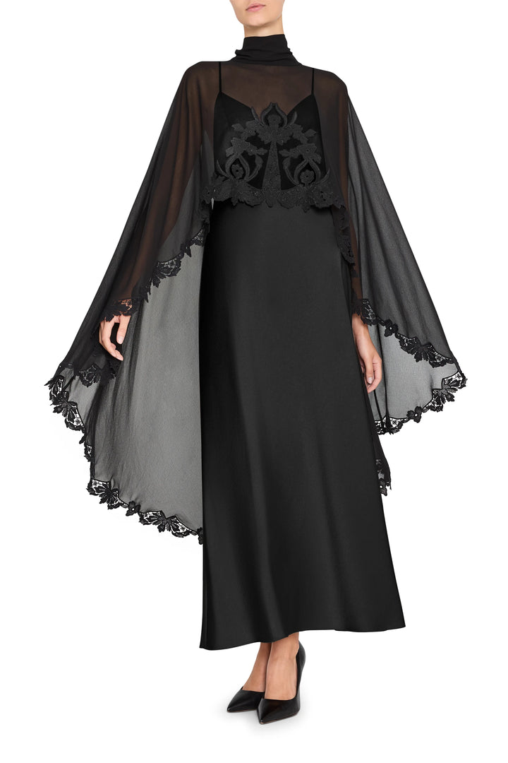 Long dress with cape, black satin-back crepe, lace trim; fitted bodice and flowing skirt. Front view on white.