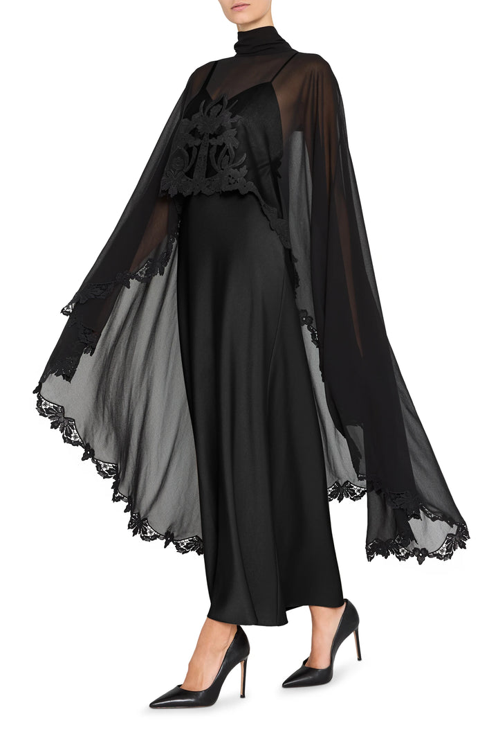 Sheer cape with lace trim over satin-back crepe long dress; fitted bodice, fluid skirt, front view on white.