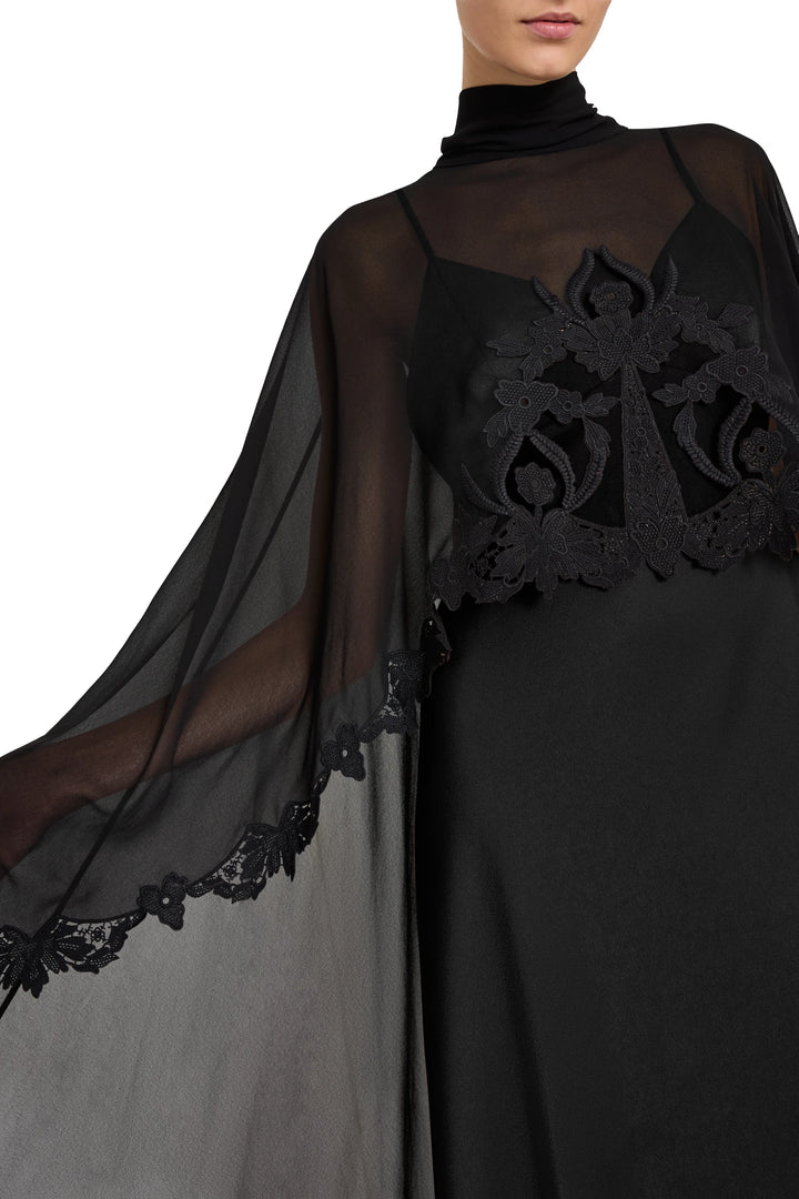 Sheer dress with cape, lace floral details, fitted bodice, fluid silhouette; front view on model.