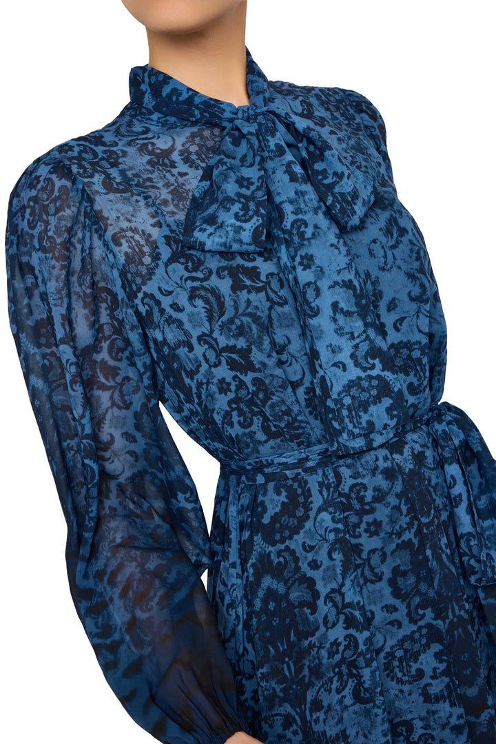 Maxi dress with bow tie neck, sheer sleeves, and floral print. Relaxed silhouette. Front view on model.
