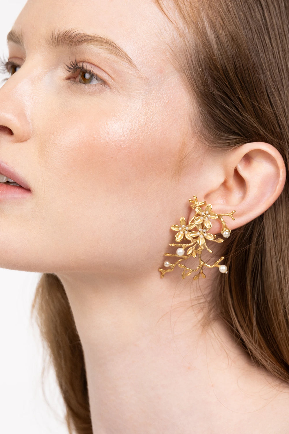 Large, gold floral ear cuffs with pearl accents, wild plant-inspired silhouette and sculpted shape, front view on model.