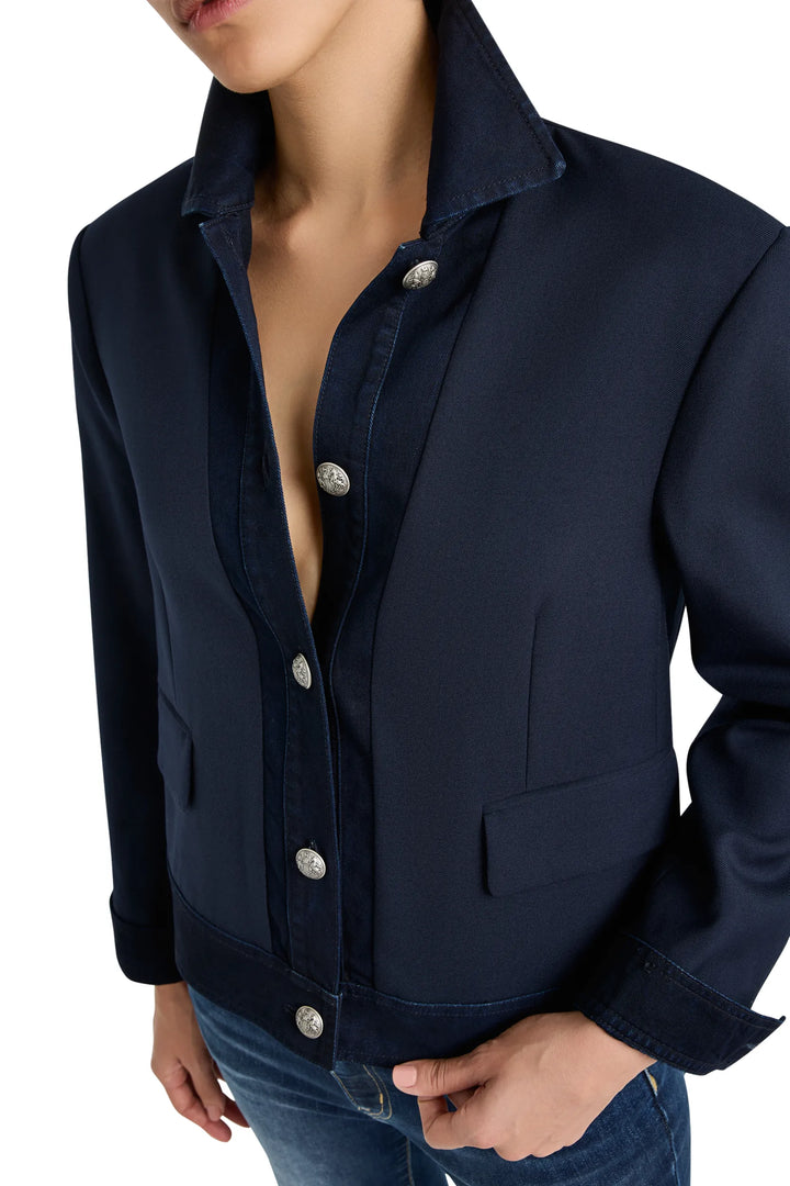 Structured denim-twill jacket with paneled construction, pointed collar, button placket; front view on white.