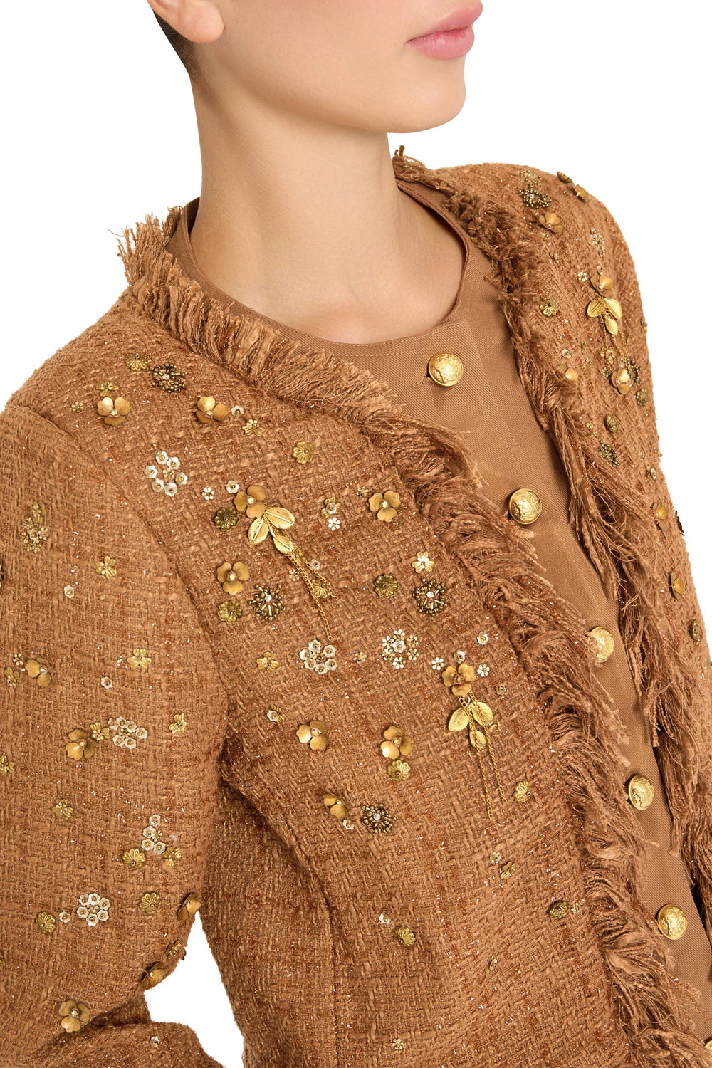Structured tweed jacket with gold buttons, fringe trim, floral accents; tailored silhouette; front view on white.