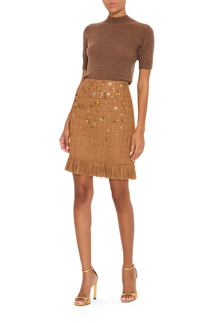 A-line tweed skirt with fringe hem and gold accents, structured fit. Front view on model.