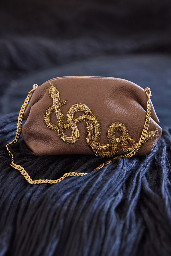 Brown handbag with gold chain strap on a dark textured surface