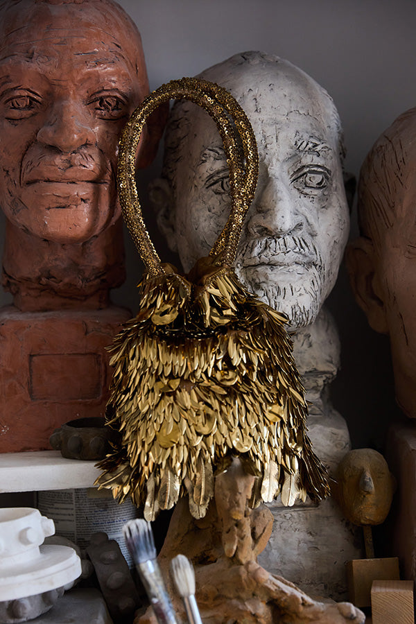 Decorative mask with gold feathers in front of a bust with a neutral expression