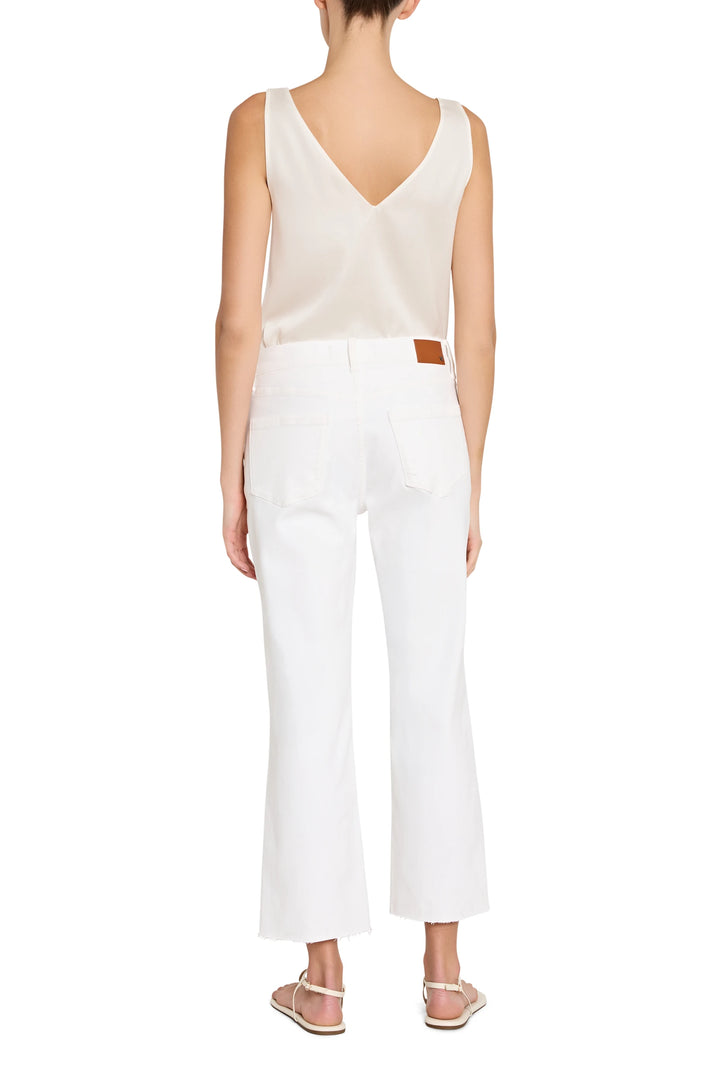 Woman wearing a beige sleeveless top and white pants on a white background