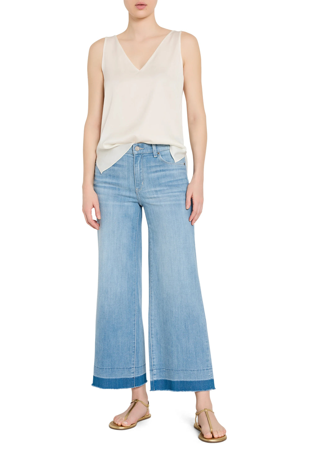 Woman wearing a cream sleeveless top and light blue wide-leg jeans on a white background