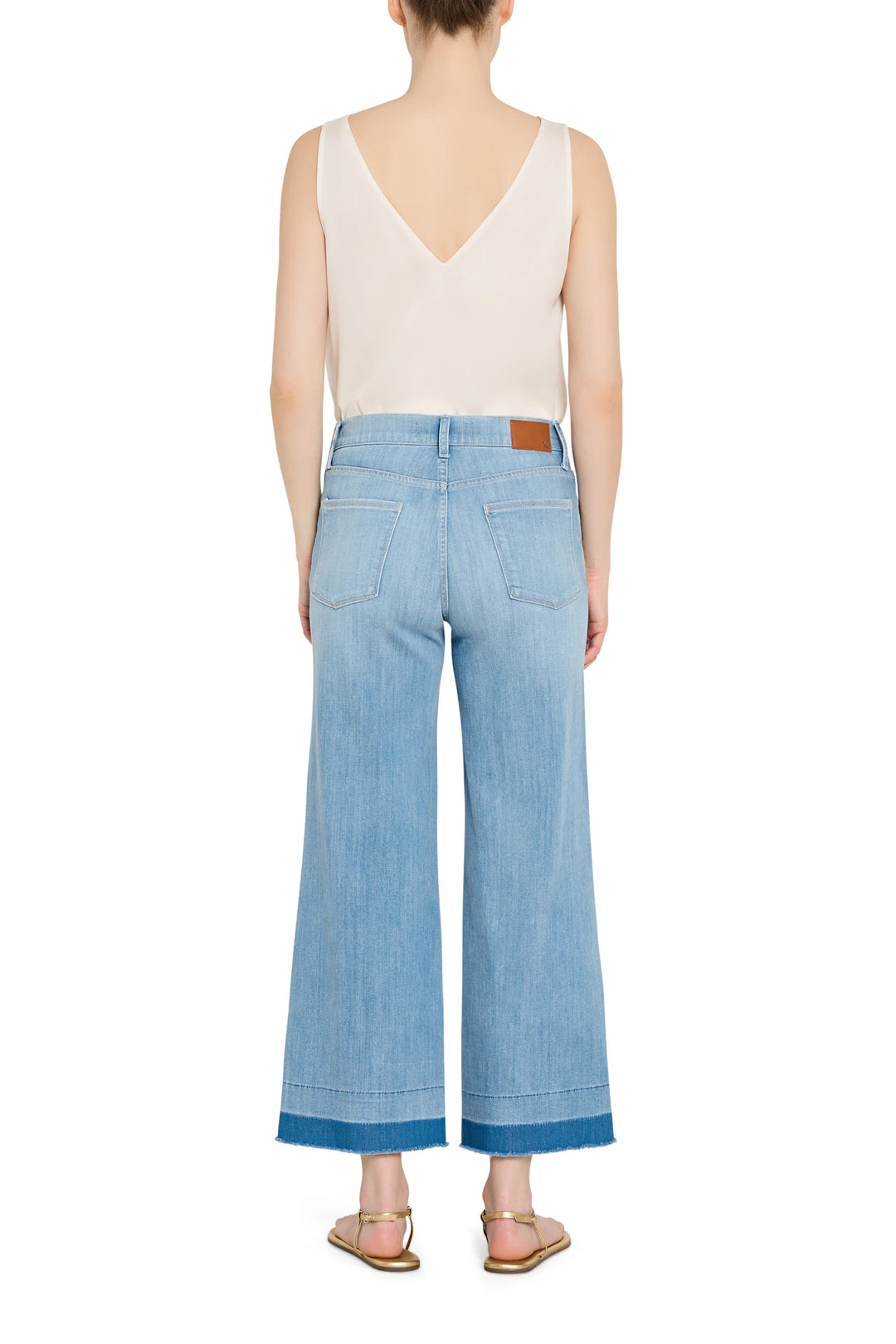 Person wearing a beige sleeveless top and light blue wide-leg jeans on a white background