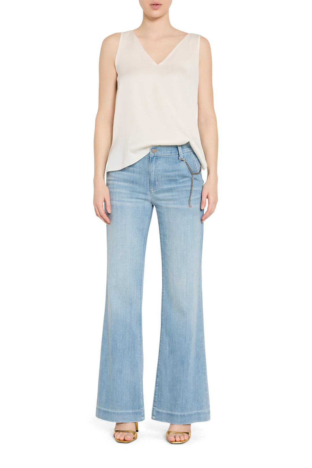 Woman wearing a cream sleeveless top and light blue flared jeans on a white background