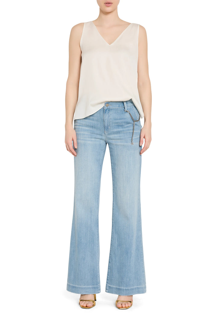 Woman wearing a cream sleeveless top and light blue flared jeans on a white background