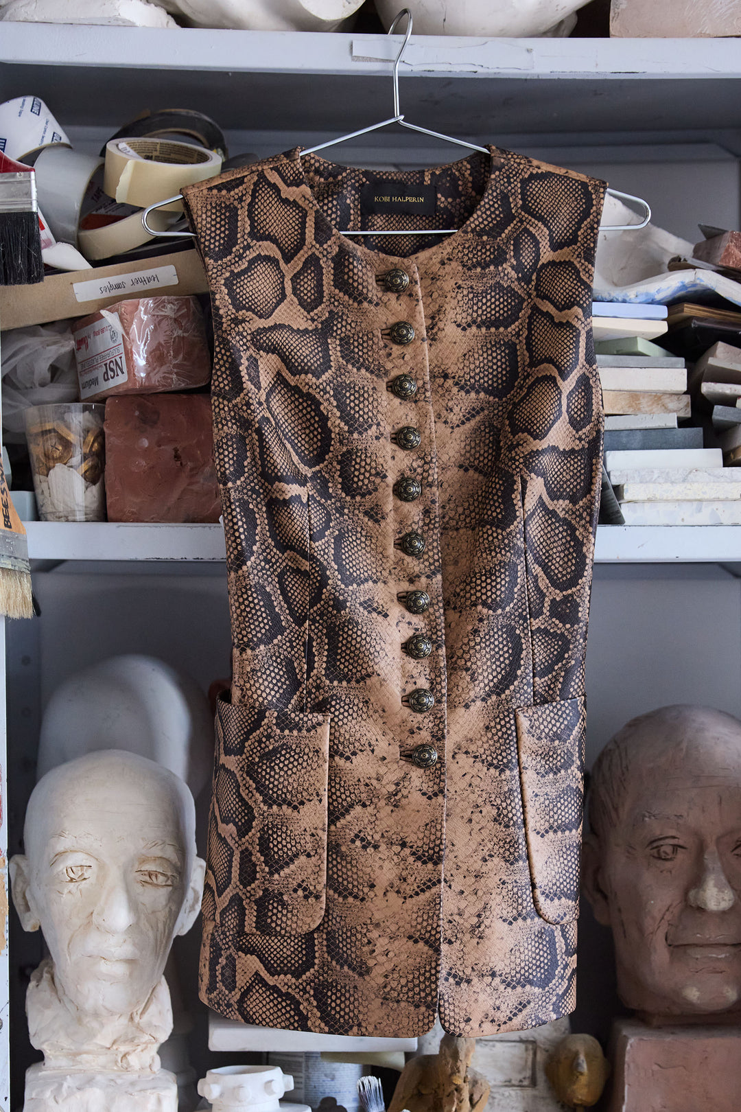 Sleeveless leather vest with antique buttons, structured fit, printed detail; front view on white.