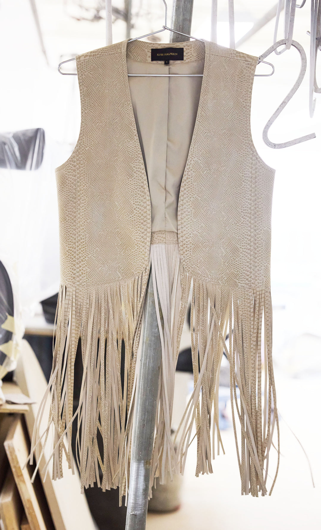 Sleeveless, straight-cut leather vest with fringe embellishment and minimal seams. Front view on white.