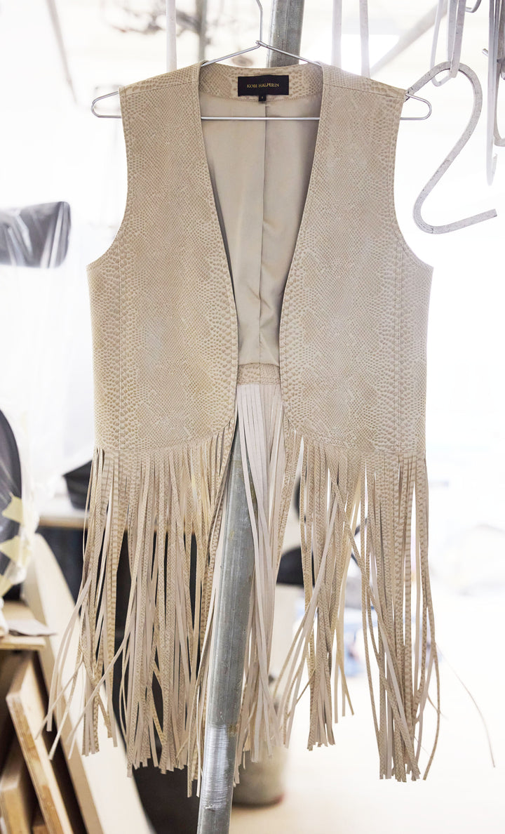 Sleeveless, straight-cut leather vest with fringe embellishment and minimal seams. Front view on white.