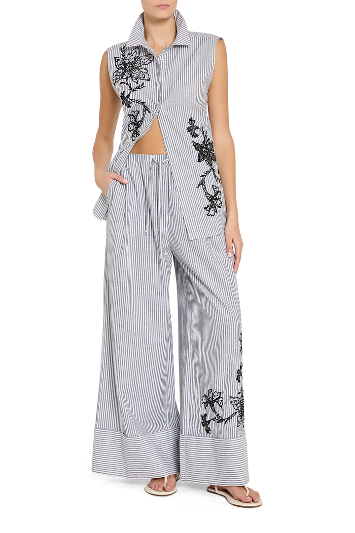 Woman wearing a sleeveless embroidered top and wide-leg pants on a white background