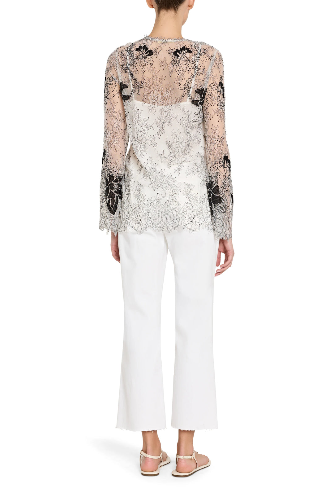 Woman wearing a floral lace top and white pants on a white background