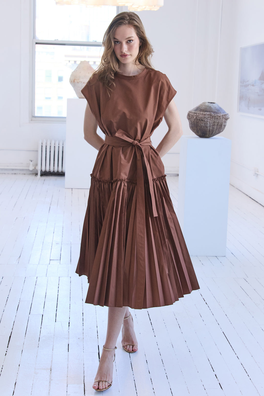 Sleeveless pleated midi dress with fitted bodice and flared skirt in smooth fabric, front view on model.
