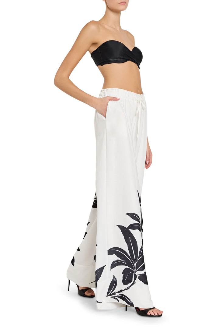 Woman wearing a black strapless top and white pants with black floral patterns on a white background