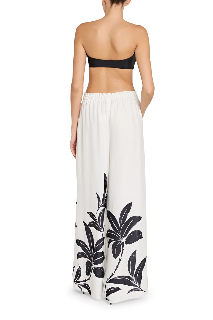 Woman wearing a strapless top and white pants with black leaf patterns on a white background