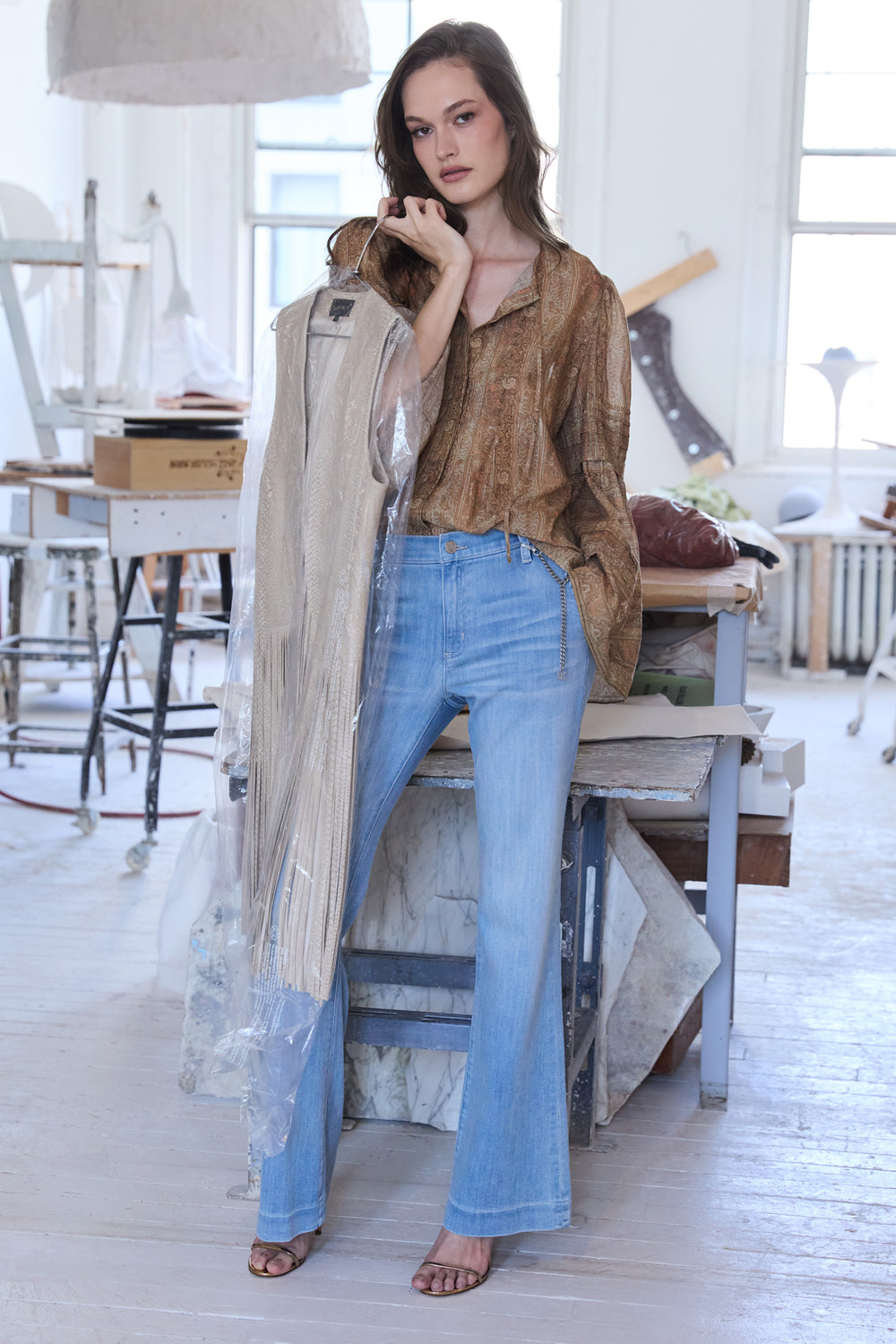 Woman wearing a brown blouse and blue jeans in a room with white walls and wooden floor.