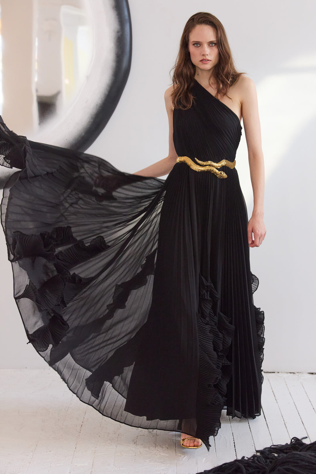 Woman wearing a black one-shoulder dress with a gold belt against a white background
