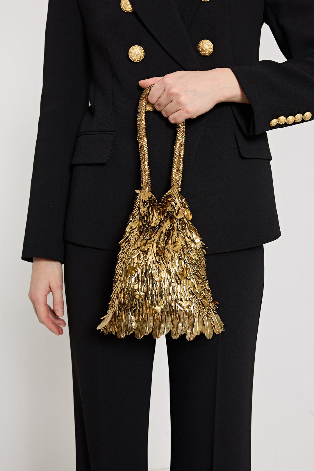 Person holding a gold sequin handbag against a plain background
