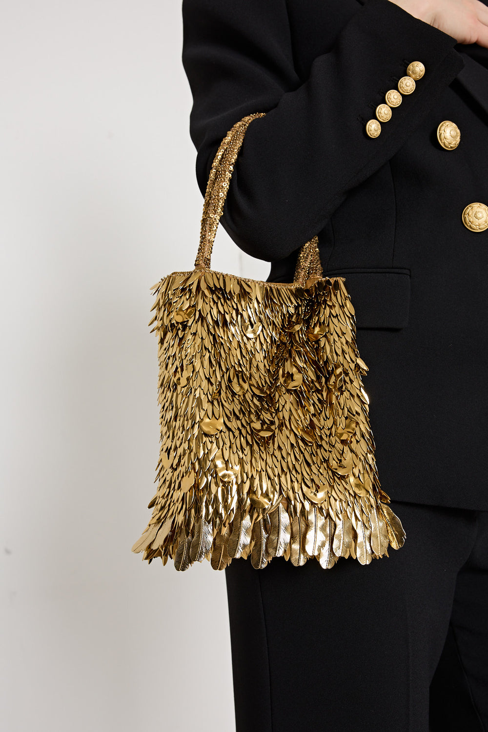 Gold sequin handbag held by a person wearing a black suit with gold buttons.