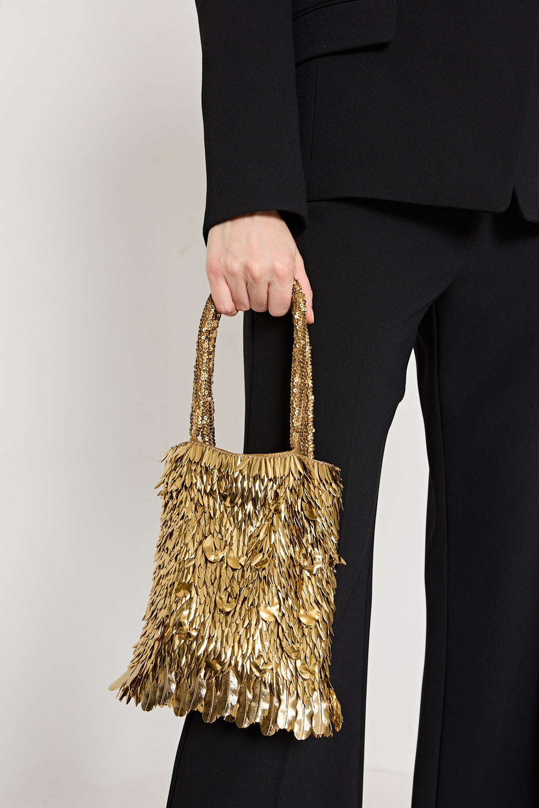 Person holding a gold sequin handbag against a plain background