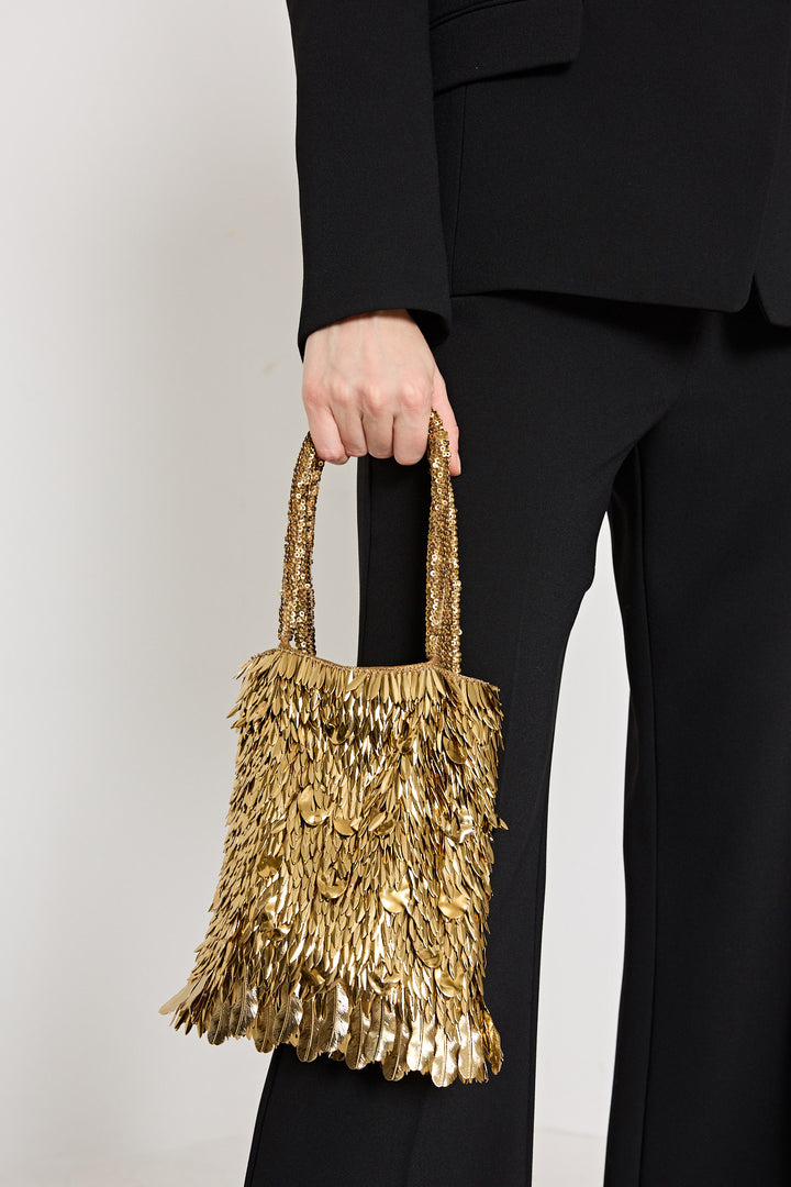 Person holding a gold sequin handbag against a plain background